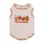 A sleeveless pet shirt in Cream with a festive autumn graphic on the front. The graphic features a coffee cup, maple leaf, football, and pumpkin above the text 'TIS THE SEASON'.